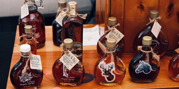Assorted glass bottles of Vermont maple syrup arranged on a wooden shelf at a local market