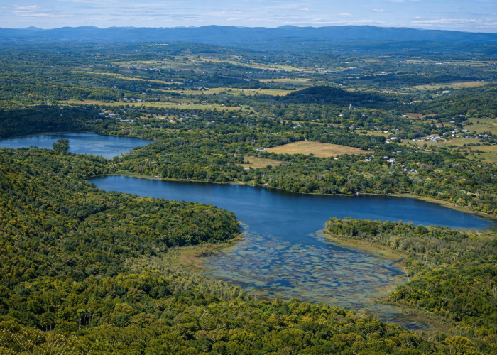Aerial view of winding lakes surrounded by forests, farmland, and rolling hills in the Hudson Valley under a clear blue sky.
