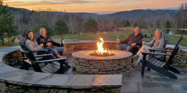 Adults relaxing around an outdoor fire pit with drinks during a Catskills brewery or tasting experience at sunset.
