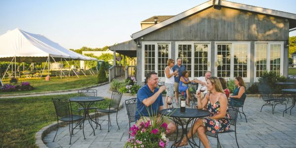 Adults relaxing around an outdoor fire pit with drinks during a Catskills brewery or tasting experience at sunset.
