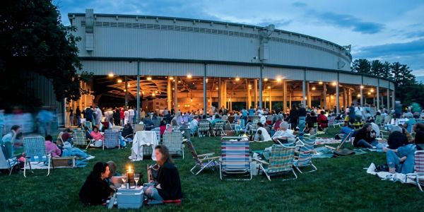 Large crowd seated on lawn chairs and blankets attending an outdoor summer concert in the Berkshires at dusk.