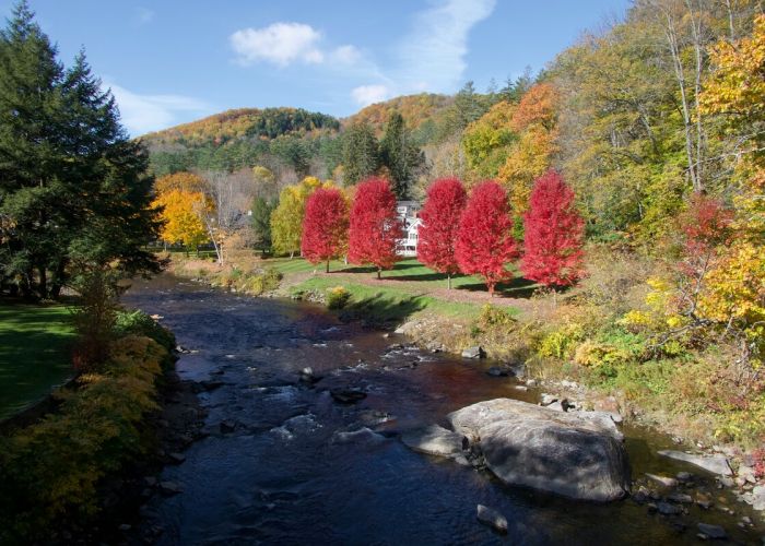 Autumn landscape in Woodstock, New York featuring a flowing river, vibrant red maple trees, and forested hills in the Catskills.