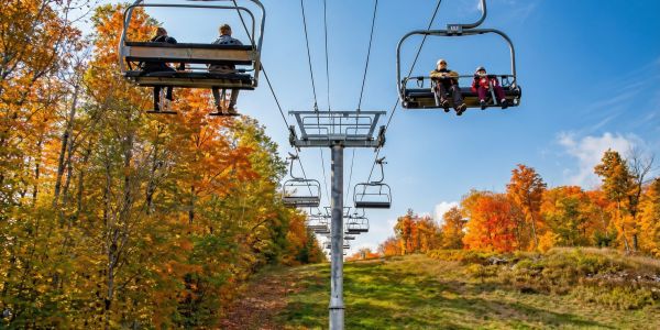 People riding a chairlift over colorful fall foliage with mountain views in the Catskills.