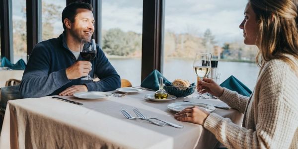 Couple enjoying a lakeside restaurant meal with wine in the Pocono Mountains during autumn.