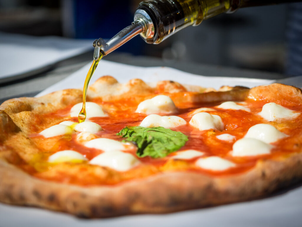 Pizza pie getting a little extra olive oil drizzled on top 